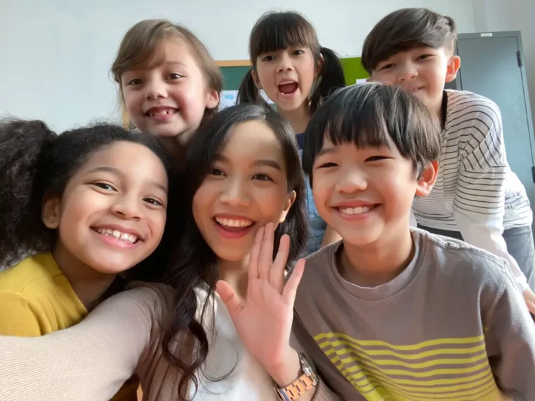 Primary school kids smiling at the camera with their English teacher