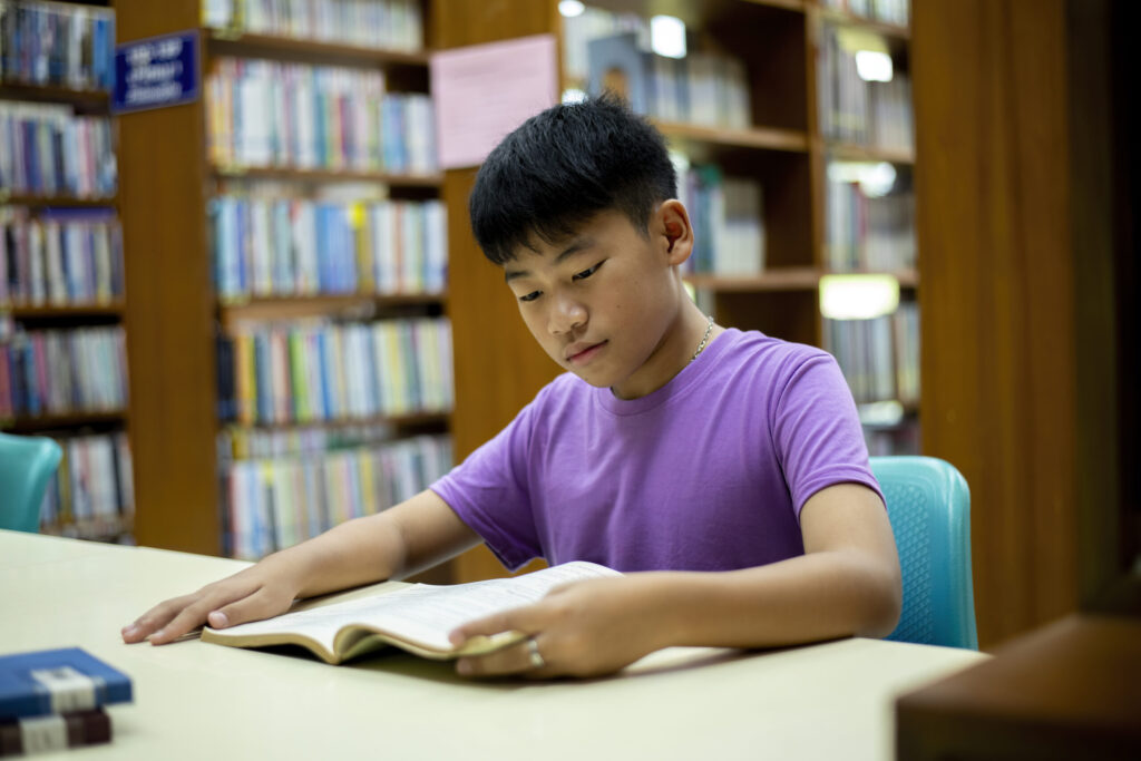 Secondary school student reading a book in a library, illustrating focused reading, critical thinking, and comprehension skills for upper secondary English.