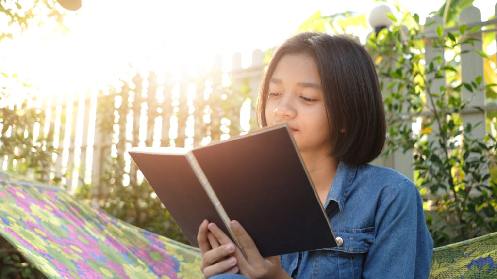Secondary 1 student reading a book outdoors, illustrating the transition from primary school reading to stronger comprehension and critical thinking skills.