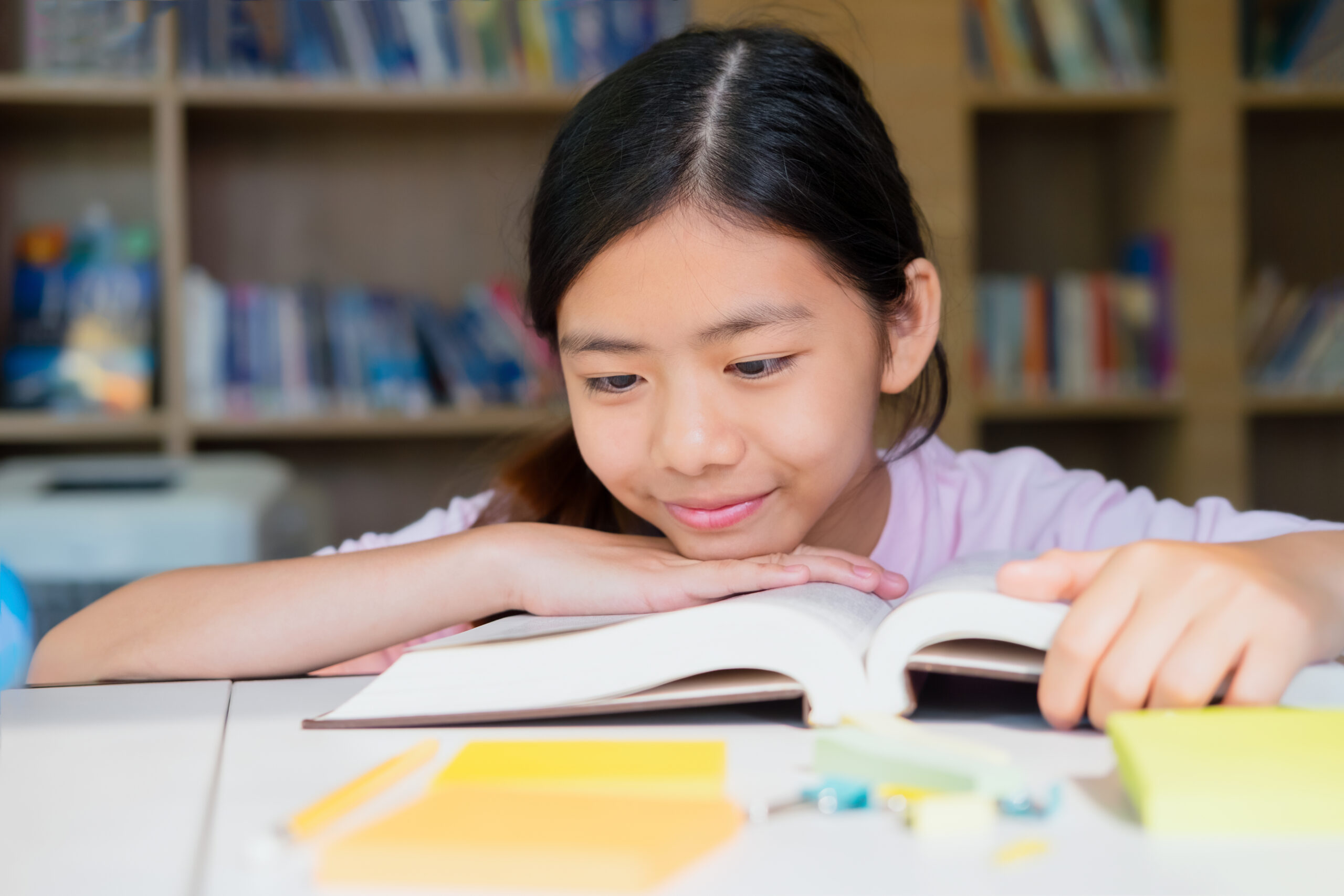 Secondary 1 student reading an open book at a library table, illustrating the development of comprehension and critical reading skills in secondary English.