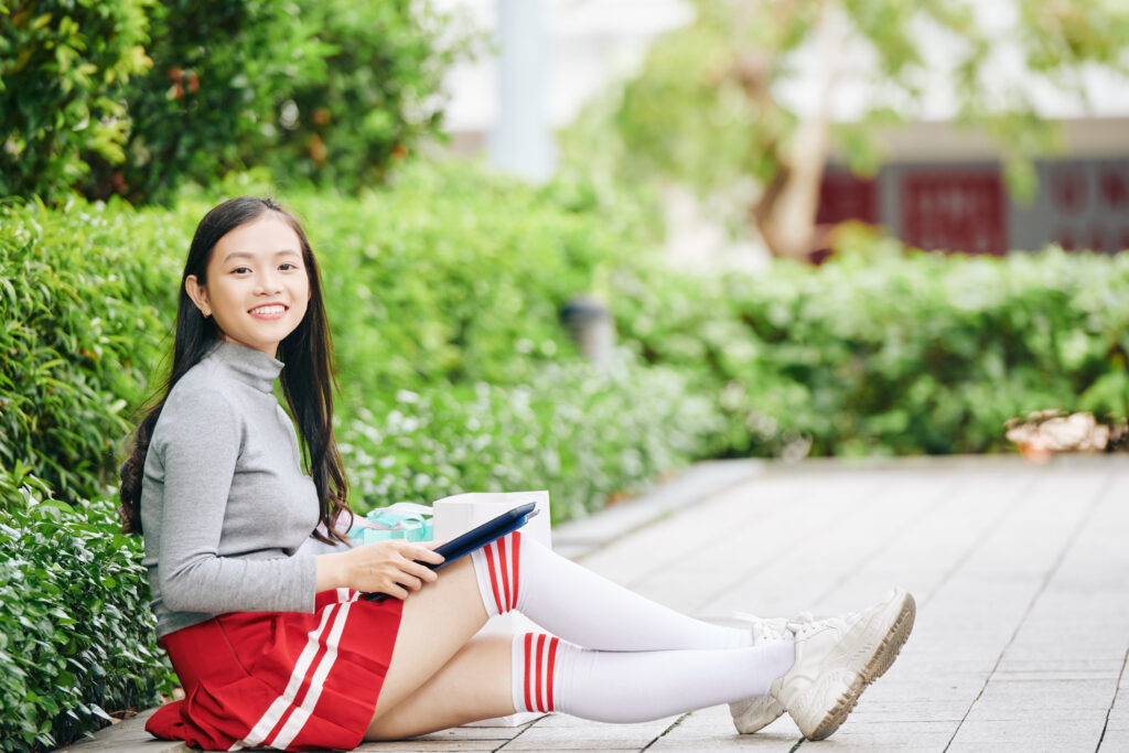 Secondary 3 student studying outdoors with a tablet, representing independent learning, critical thinking, and preparation for upper secondary English and the O-Level examinations.